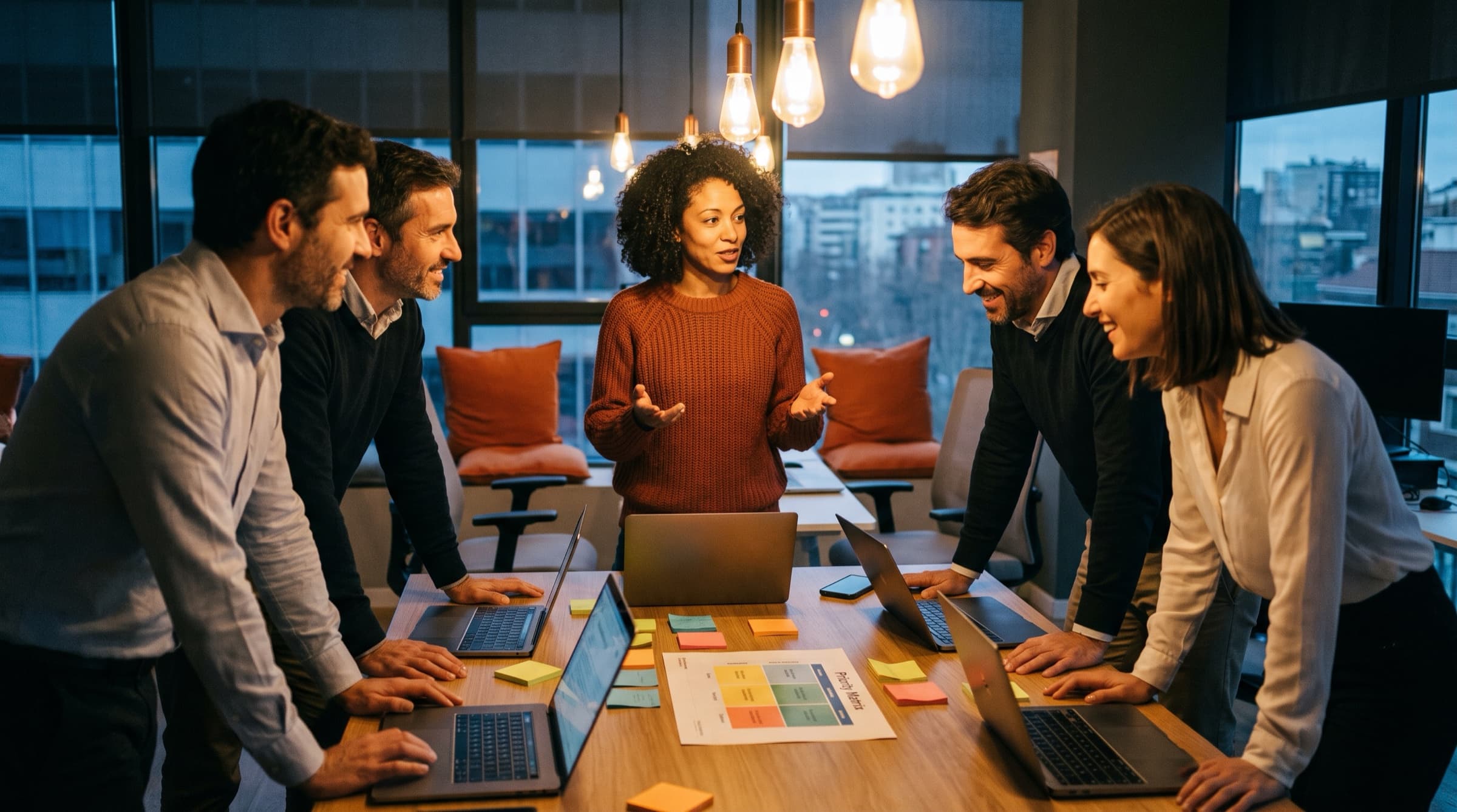 Equipo de producto trabajando en un taller de IA alrededor de una mesa con portátiles y una matriz de prioridades